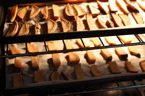 Sweet potato wedges roasting in the oven, spaced out evenly on two cookie sheets