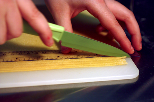 pasta being hand cut using a ruler's edge on a cutting board
